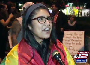 A young woman wearing a rainbow flag is among the those at a protest against the Donald Trump presidency at Alamo Plaza on November 11. (Video capture via KSAT-TV)